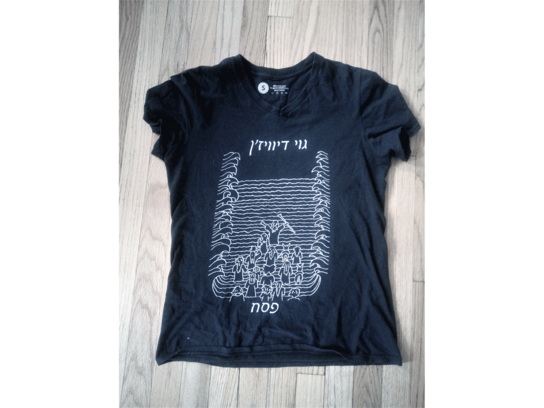 The artwork titled "Goy Division" was created in 2016 by Jacob Rath. The image is a black t-shirt with a white line drawing of Moses parting the Red Sea. The artwork was made with a cotton t-shirt and ink, and is 26 inches by 24 inches.