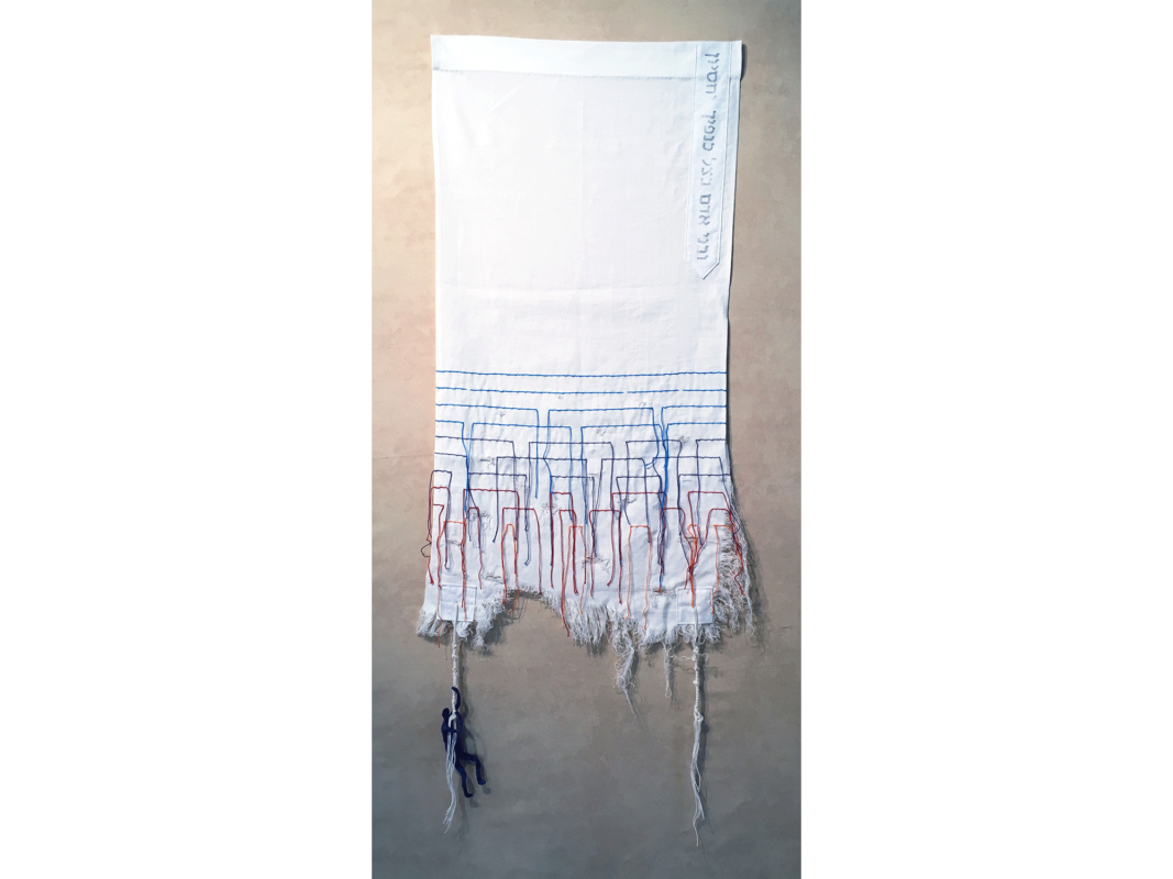 The artwork titled "Hanging by a Thread" was created in 2018 by Heather Stoltz. The image is a rectangular white piece of fabric mounted on a white wall. A combination of blue, black, and red threads are woven throughout the lower part of the piece, and the embroidered lines are broken and frayed at the ends. The artwork is a textile piece that incorporates cotton fabrics, cotton, string, polyester stuffing, and wire. The piece is 47 inches long and 18.5 inches wide.