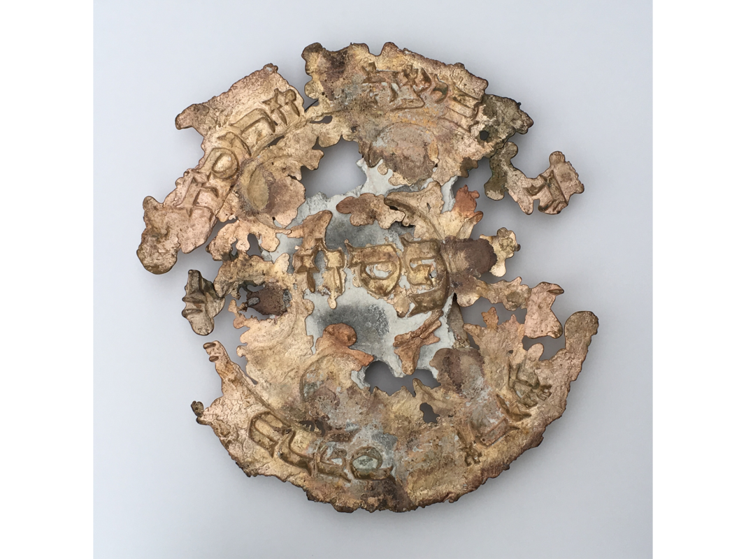 The artwork "Seder Plate" was created in 2019 by Barry Goldstein as part of Goldstein's Artifact series. The image is an eroded bronze seder plate carved with faded Hebrew text. The plate's edges interior surfaces appear to have been corroded away. The artwork is a bronze sculpture, 22 inches by 22 inches.