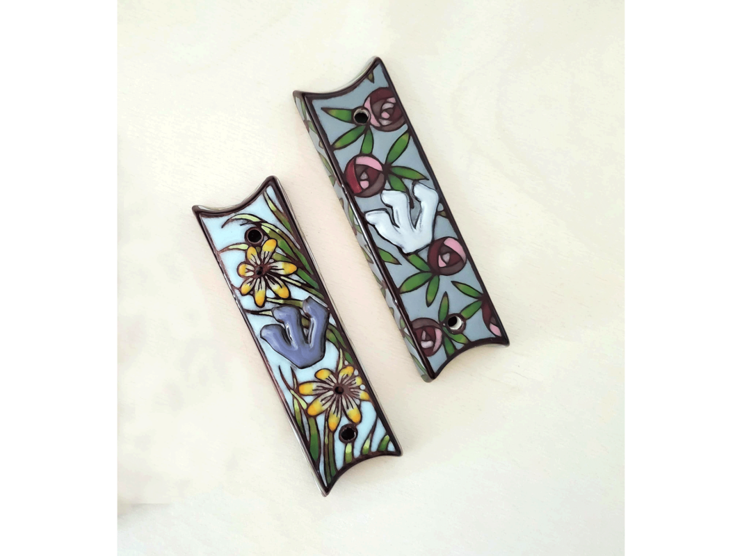The artworks "Black-Eyed Susans mezuzah" and "Roses mezuzah" were created in 2019 by Bonnie Zuckerman. The "Black-Eyed Susans mezuzah" shows yellow Black-Eyed Susan flowers and blades of green grass against a pale blue sky. The "Roses mezuzah" shows perfectly round pink and red roses and green leaves against a pale blue sky. The artworks are hand-painted ceramics with wax resist. Each mezuzah measures 4.75 inches tall, 1.25 inches wide, and 0.5 inches deep.
