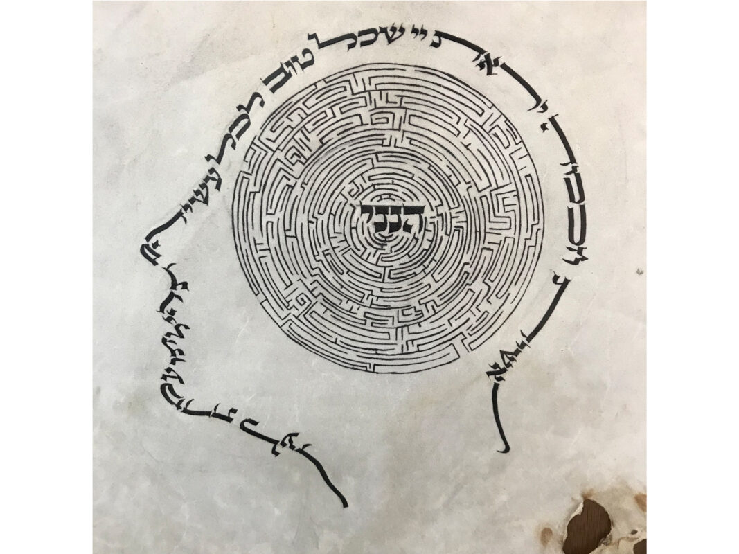 This artwork titled "Identity" was created in 2016 by Kalman Gavriel Delmoor. The image is an outline of human head in profile, and the lines of the drawing are Hebrew text. Inside the head is a maze with at the middle the Hebrew word "heineni," meaning "Here I am." The artwork is black ink on parchment, 42 by 35 centimeters.